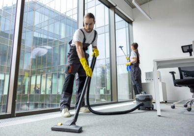 Vacuum cleaning. Young man in uniform vacuum cleaning the floor in the conference room